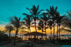 a beach with palm trees and tables and a sunset at Pousada Jagatá in Tutóia