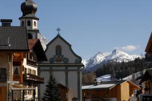 a building with a clock tower with mountains in the background at Hotel Falzares in San Cassiano