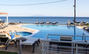 a swimming pool with people laying in chairs next to the ocean at Blue Waves Apartments in Plomarion