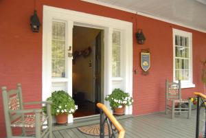 een veranda van een rood huis met twee stoelen en een deur bij Le Passe-Partout in Cowansville