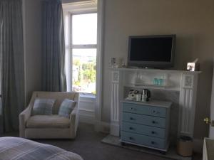 a bedroom with a television and a dresser with a chair at Alberta Guest House in Dundee