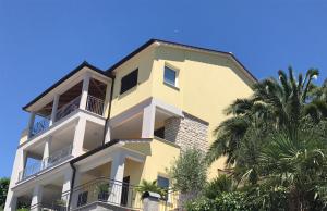 a yellow building with balconies and a palm tree at Apartments Supra Mare in Rabac