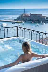 a woman sitting in a hot tub overlooking the ocean at Hotel Riva by Aycon in Petrovac na Moru