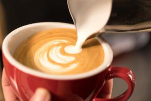 a person is pouring milk into a cup of coffee at Swiss Hotel Apartment in Kuala Belait