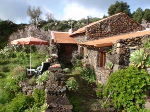 a stone house with an umbrella and some plants at Casa rural La Jarita in El Pinar del Hierro