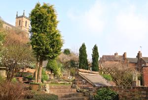 a garden with a brick wall and trees and a church at The Library House B&B in Ironbridge