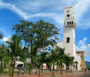 a clock tower in front of a building with palm trees at Hotel El Triangulo in Pitalito