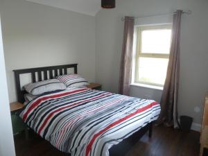 a bedroom with a bed with a striped comforter and a window at Mary's Meadow in Doolin