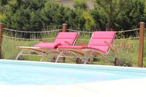 2 chaises roses assises à côté d'une piscine dans l'établissement Hôtel Restaurant La Désirade, à Saint-Désirat