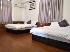 two beds in a room with wooden floors and curtains at Lu He Feng Homestay in Luodong