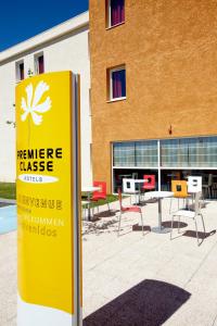 un panneau jaune devant un bâtiment avec des tables et des chaises dans l'établissement Première Classe Istres, à Istres