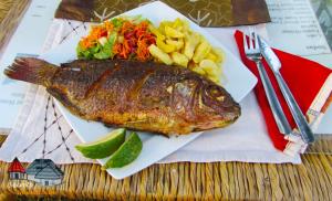 a fish on a plate with chips and vegetables at Secrets Guest House in Entebbe +41 photos