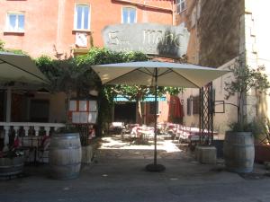 un patio con sombrilla, mesas y sillas en Hôtel Restaurant le Saint Marc, en Aups