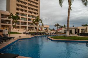 une piscine bordée de palmiers et un bâtiment dans l'établissement Ocean View Beach Hotel, à Mazatlán