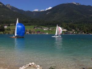 two sailboats on a lake with mountains in the background at Loitzbauer Ferienwohnungen in Sankt Gilgen