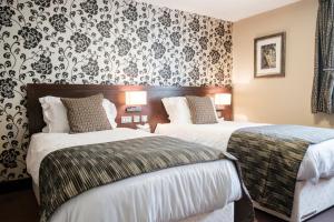 two beds in a hotel room with floral wallpaper at The Hampshire Hog in Clanfield