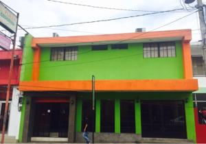 a green building with a person walking in front of it at Hotel Plaza Cosiguina in Chinandega