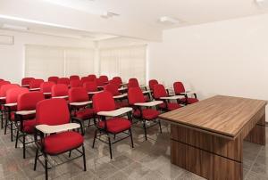 una sala de conferencias con sillas rojas y un podio de madera en Hotel Dois H, en Joinville 19 fotos más