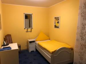 Habitación pequeña con cama amarilla y escritorio. en Gasthaus Metzgerei Pension Maßem en Schillingen