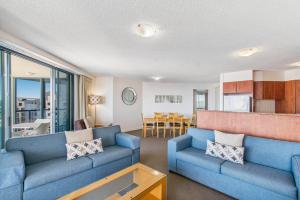 a living room with blue couches and a kitchen at Mantra Mooloolaba Beach in Mooloolaba