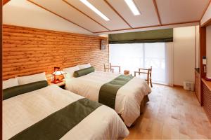 two beds in a room with a wooden wall at Hotel Fuki no Mori in Nagiso