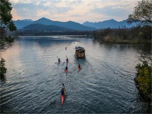a group of people are rowing a boat on a river at Yurong West Lake Cottage Resort Hotel Hangzhou in Hangzhou