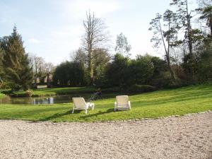 two white chairs sitting in the grass near a pond at Les Poteries in Fresville