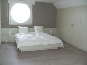 a white bedroom with a white bed and a window at 't Vossenerf in De Haan