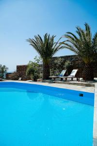 a blue swimming pool with two chairs and palm trees at Villa Melydia in Koundouros +21 photos