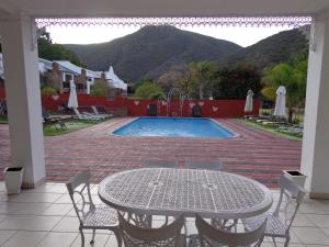 eine Terrasse mit einem Tisch, Stühlen und einem Pool in der Unterkunft De Oude Meul Country Lodge & Restaurant in Oudtshoorn