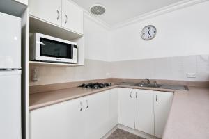 La cuisine est équipée de placards blancs et d'un four micro-ondes. dans l'établissement Lorhiti Apartments, à Lord Howe