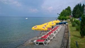 a row of beach chairs with umbrellas next to the water at Hotel Dva Bisera in Ohrid