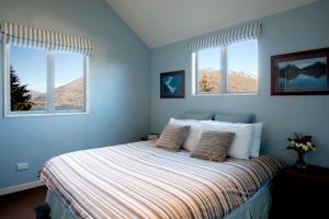 ein blaues Schlafzimmer mit einem Bett und zwei Fenstern in der Unterkunft White Peaks Villa in Queenstown