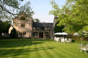 Biggin Hall Country House Hotel في هارتنغتون: منزل حجري قديم مع كراسي ومظلات على عشب