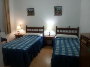 two beds in a room with two lamps on tables at Pensión Ciudad Navarro Ramos in Granada