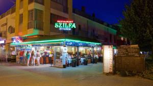 a group of people standing outside of a restaurant at night at Szilfa Étterem Mariann Apartman in Hajdúszoboszló