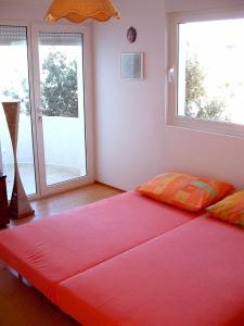 un grande letto rosso in una stanza con due finestre di Apartments Roko a Mali Iž