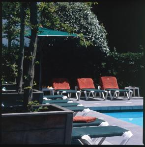 2 chaises longues et une piscine avec des chaises rouges dans l'établissement Romantik Manoir Carpe Diem, au Coq