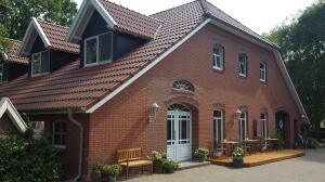 a red brick building with a white door at Pension am Birkensee in Detern