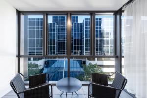 einen Glastisch und Stühle in einem Zimmer mit Fenstern in der Unterkunft SKYE Hotel Suites Parramatta in Sydney