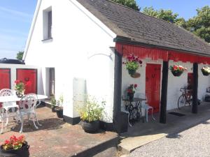 a white building with red doors and a table and chairs at Cummins Cottages in Ballycrossaun
