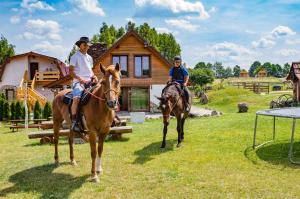 dos personas montando caballos delante de una casa en Osada Łagówek - domek letniskowy do wynajęcia en Łagów