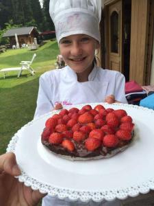 Een jong meisje met een taart met aardbeien erop. bij B&B Maso al Cervo in Fiera di Primiero