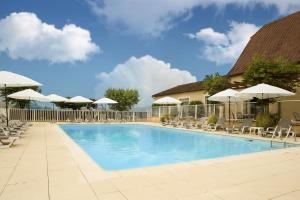 una gran piscina con sillas y sombrillas en L'Oustal de Vézac, en Vézac