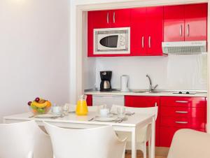 a kitchen with red cabinets and a white table and chairs at H10 Suites Lanzarote Gardens in Costa Teguise