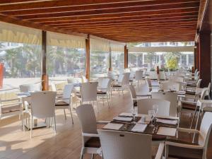 a restaurant with white tables and chairs and windows at H10 Suites Lanzarote Gardens in Costa Teguise