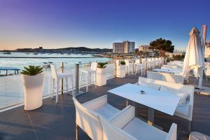 a row of tables with white chairs and umbrellas at Marina Playa Hotel Apartments by Typic Hotels - Adults Only in San Antonio Bay