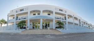 a large white building with palm trees in front of it at Donnosanto Residence Torre Santa Sabina in Torre Santa Sabina