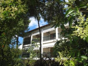 a white building with a balcony in the middle of trees at Alexander in Pefkochori