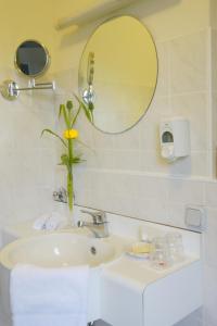 lavabo con espejo y jarrón con flor amarilla en Trans World Hotel Auefeld, en Hannoversch Münden